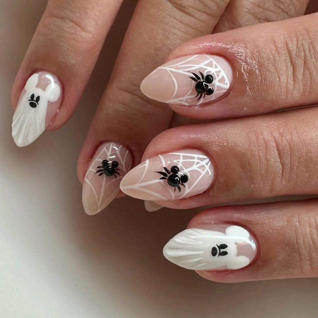 Hand with custom press-on nails featuring white spider web and ghost designs, black spider art