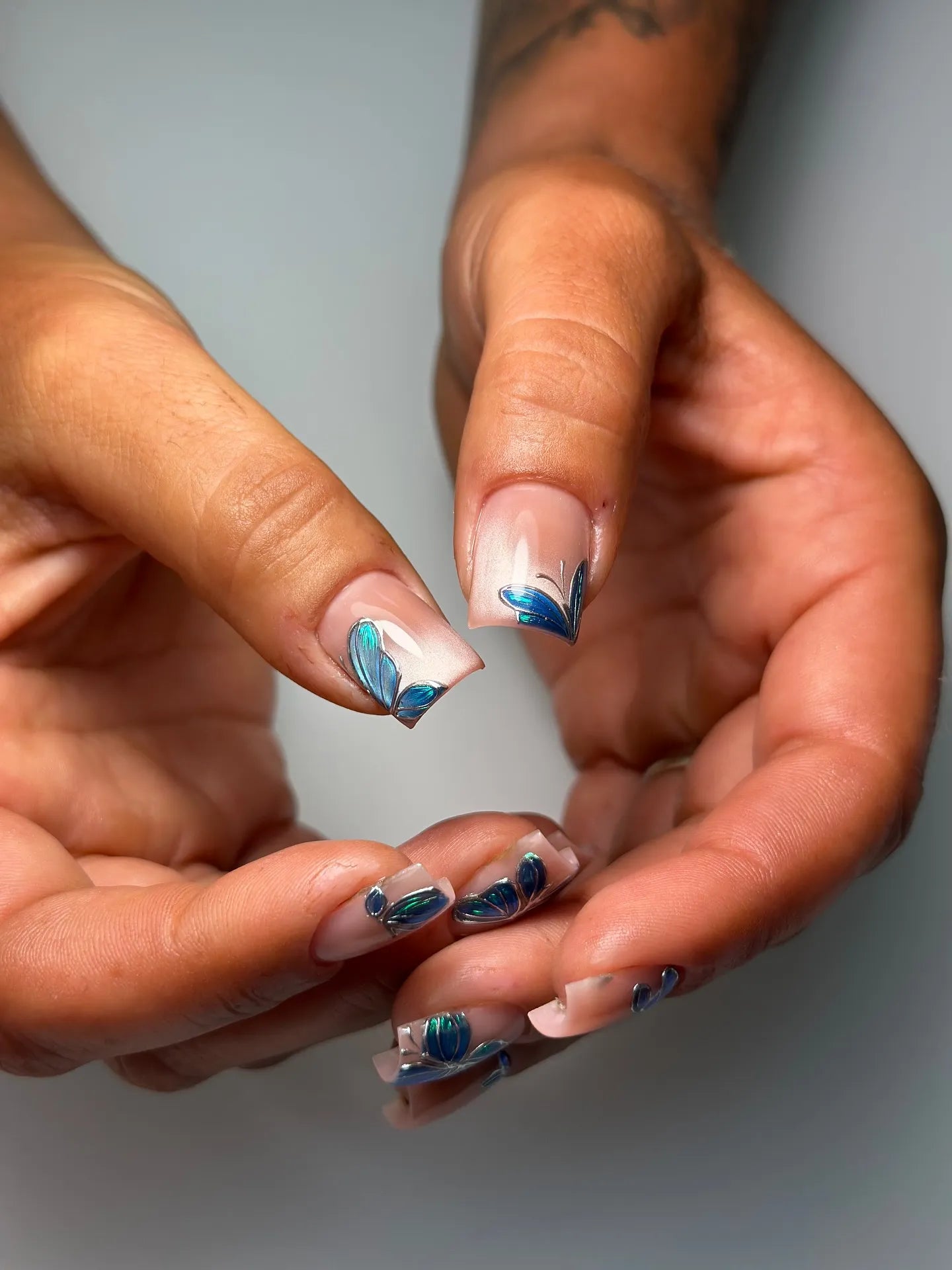 Hand with nude base press-on nails featuring 3D blue butterfly and chrome accents.
