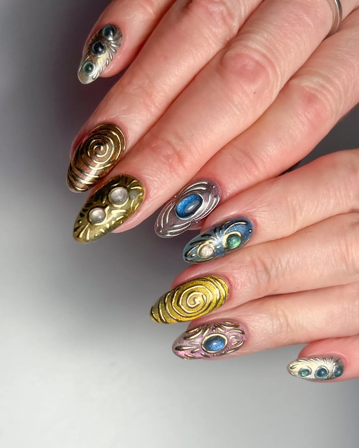 Hand with handmade 3D metallic press-on nails featuring gemstone and ancient artifact designs.