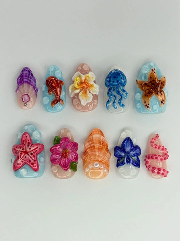 Handmade press-on nails with 3D ocean reef designs, featuring starfish, jellyfish, flowers, shells, and tropical sea creatures on pastel backgrounds.