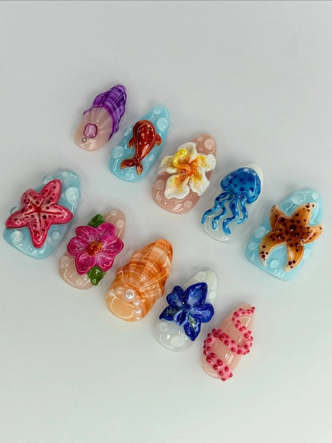 Handmade press-on nails with 3D ocean reef designs, featuring starfish, jellyfish, flowers, shells, and tropical sea creatures on pastel backgrounds.