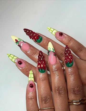 Hand with long press-on nails featuring 3D strawberry, ladybug, and gingham plaid summer designs.