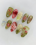 Handmade press-on nails with pink orchid floral designs, greenery accents, and 3D artistic details.