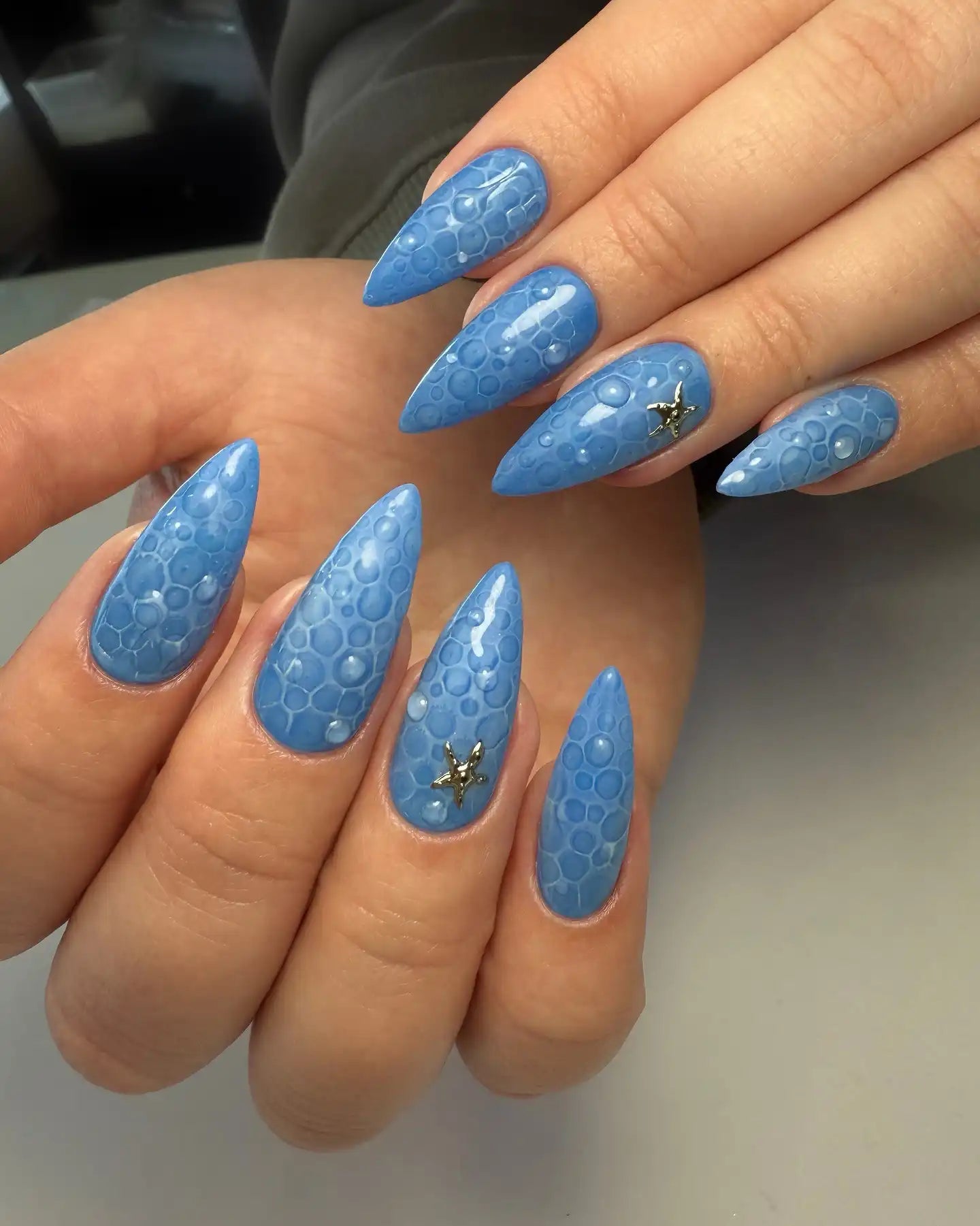 Hand with blue bubble textured 3D press-on nails featuring small starfish accents