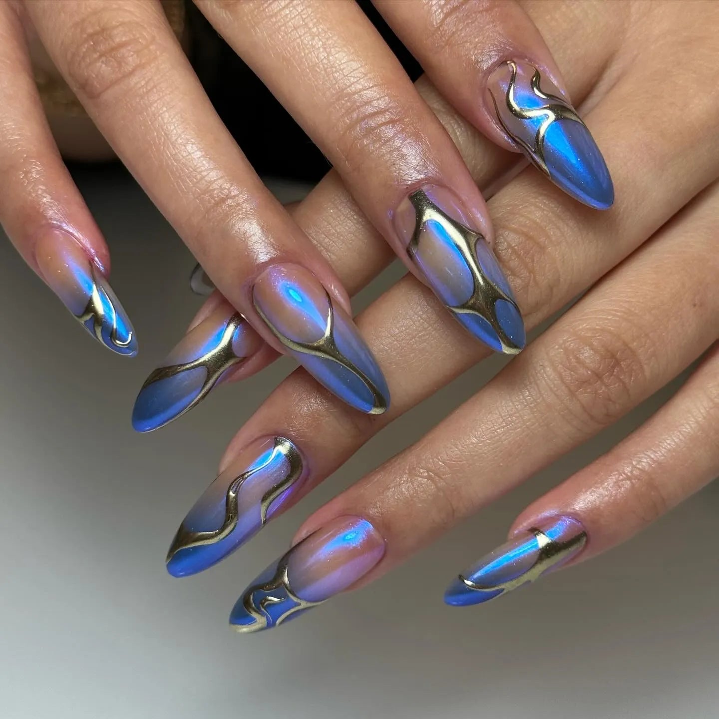 Hand with long coffin-shaped press-on nails in metallic blue with chrome abstract accents