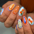 Handmade Mediterranean-inspired press-on nails with orange fruit, blue fish, and artistic patterns