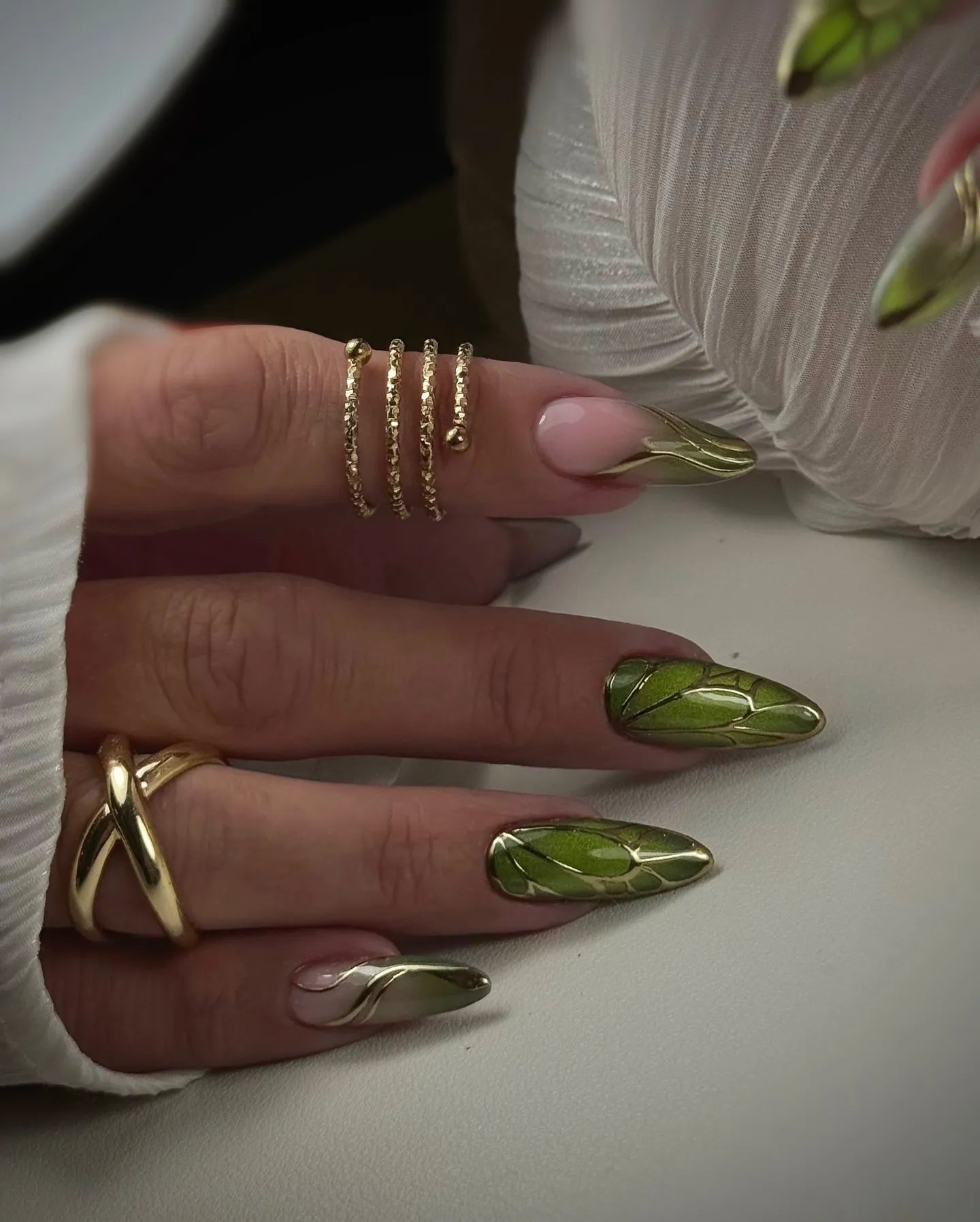 Hand with handmade green beetle wing press-on nails and gold chrome accents