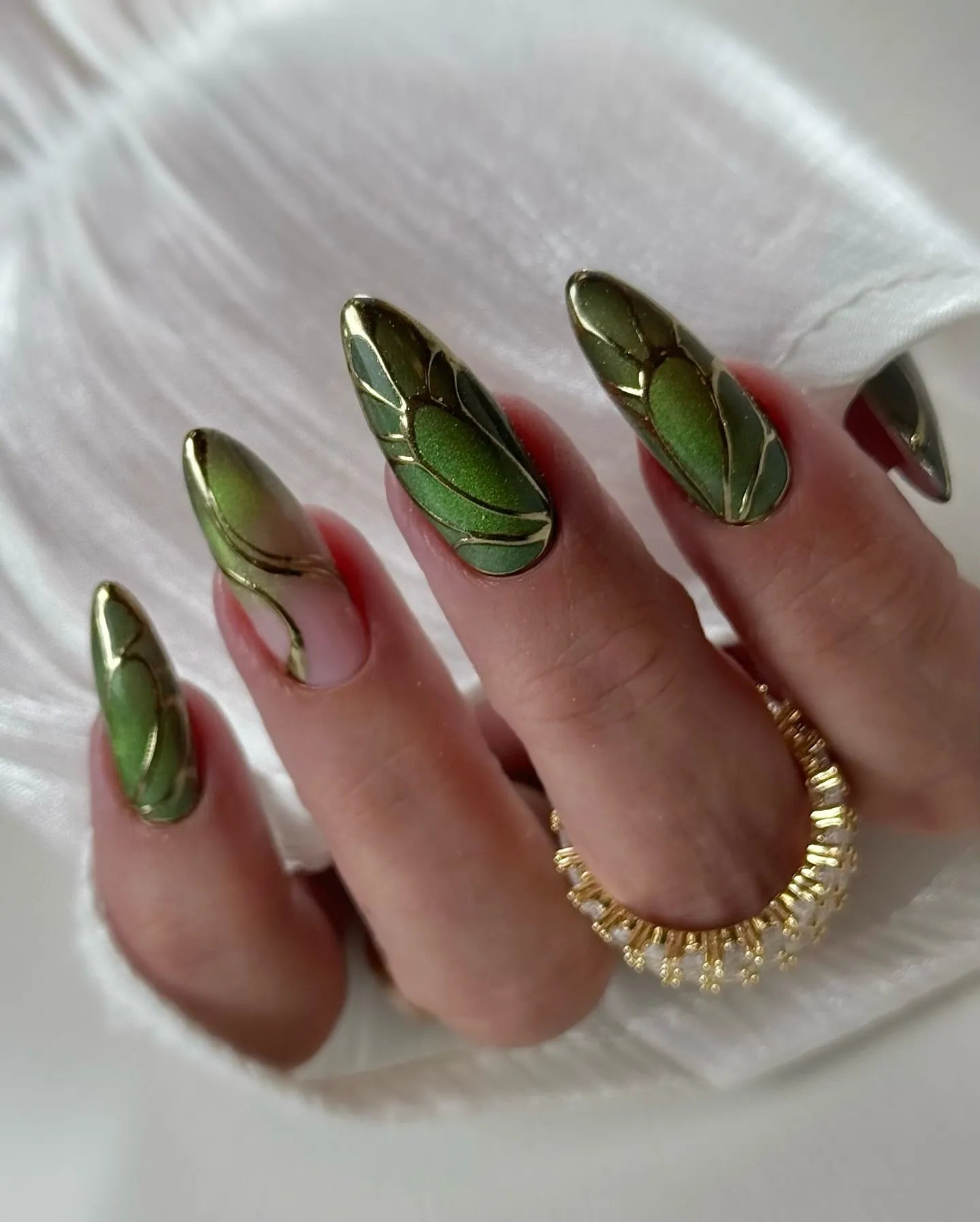 Hand with long handmade press-on nails, green beetle wing design and gold chrome accents