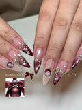 Hand with long stiletto press-on nails, burgundy metallic design, silver bow and gem accents.
