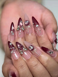 Handmade burgundy stiletto press-on nails with silver bows, gems, and festive metallic accents.