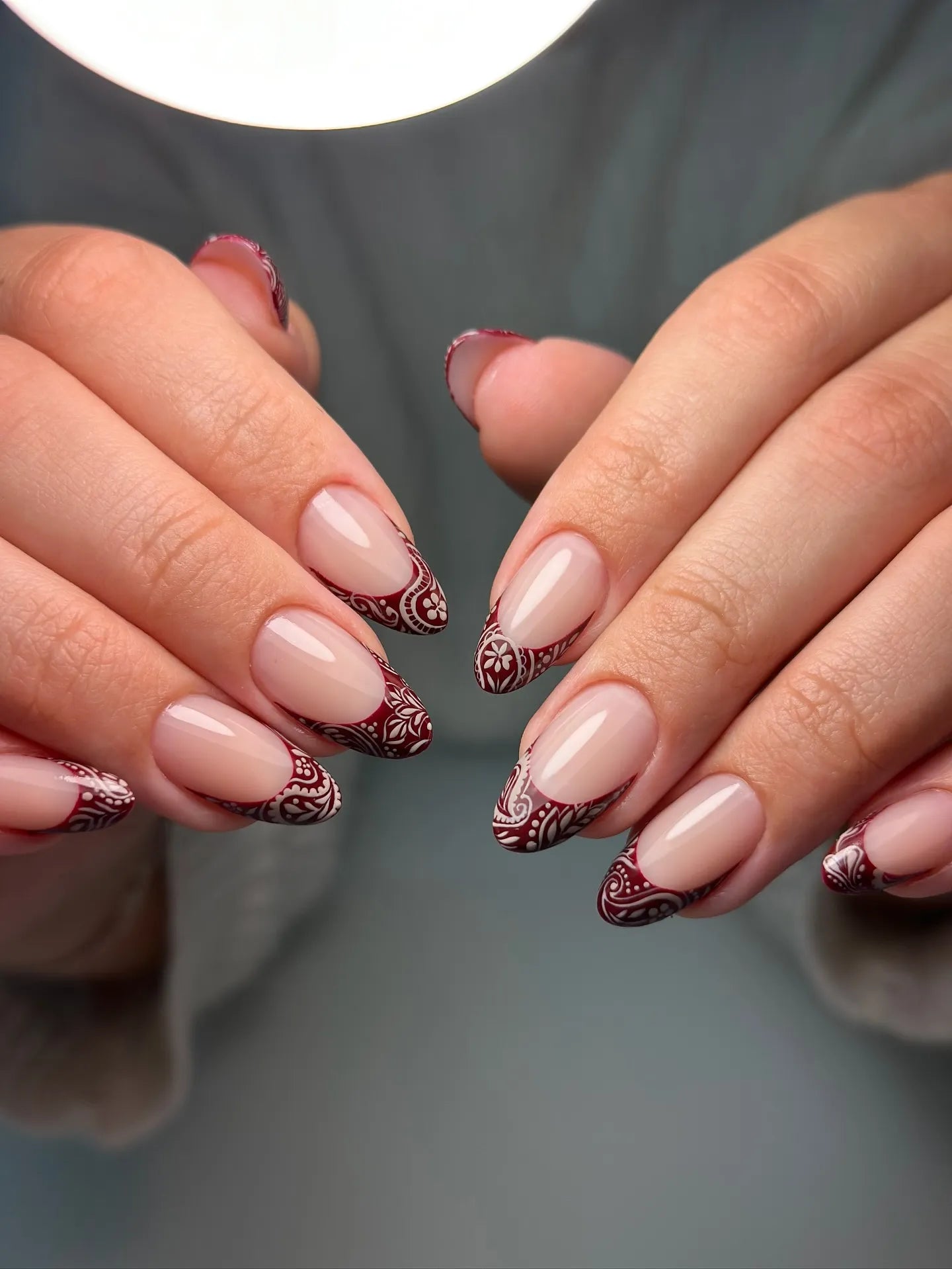 Handmade press-on nails with burgundy lace French tips and mandala designs on a nude base.