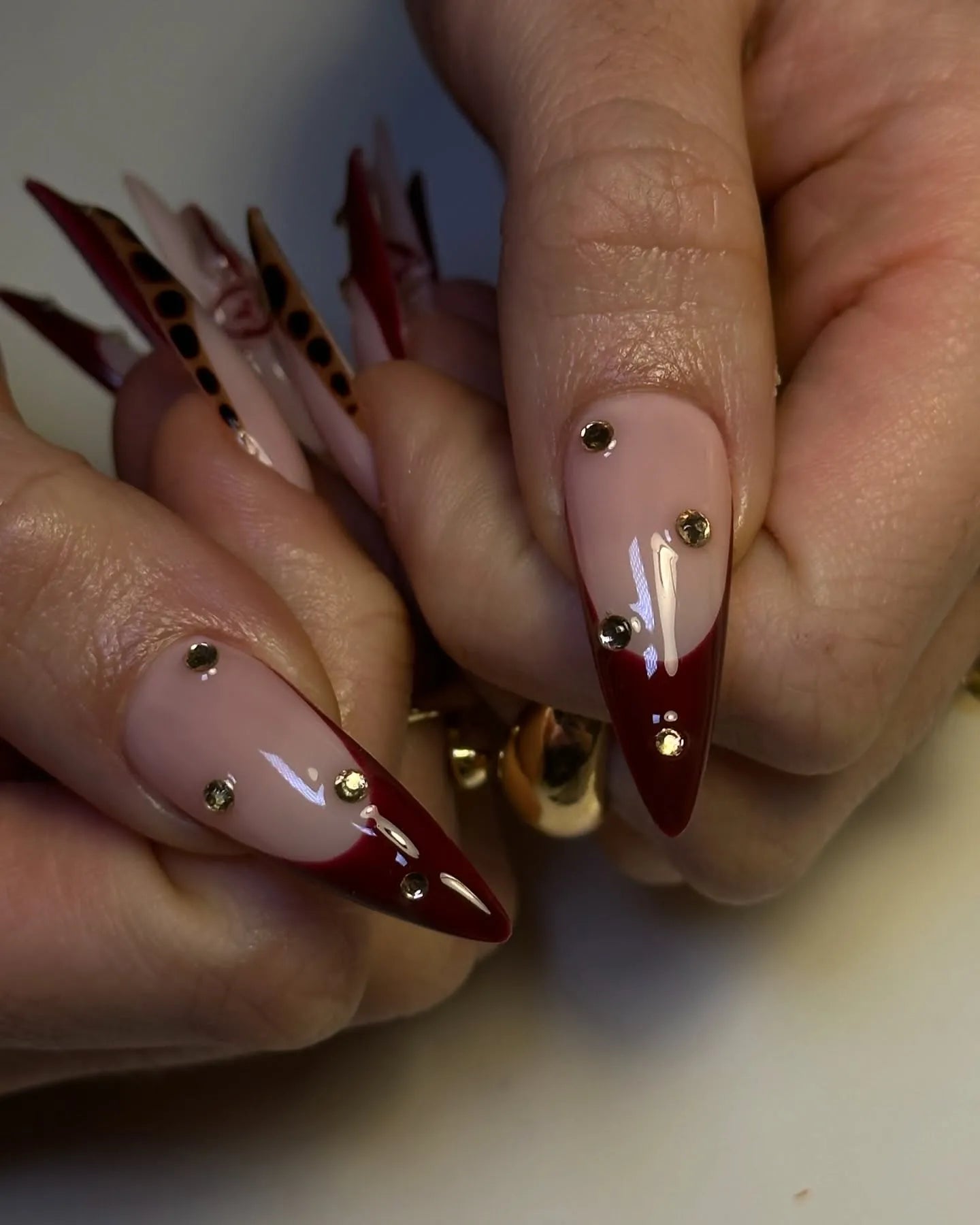 Handmade press-on nails with burgundy red tips, leopard print, and gold rhinestone accents.