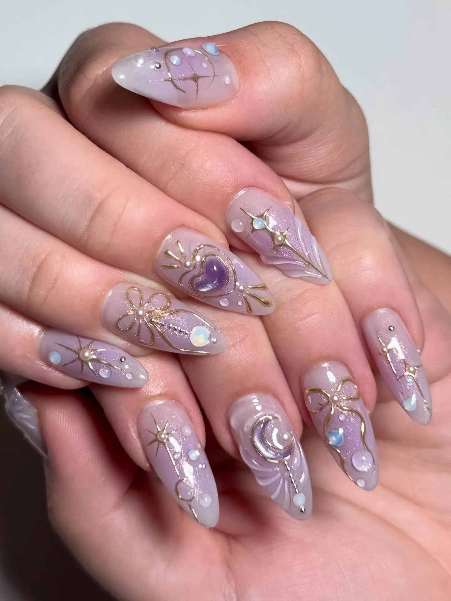 Handmade stiletto press-on nails with purple heart, gold bow, crescent moon, and star designs