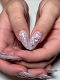 Hand with handmade press-on nails, featuring purple heart, gold bow, celestial and pearl accents.