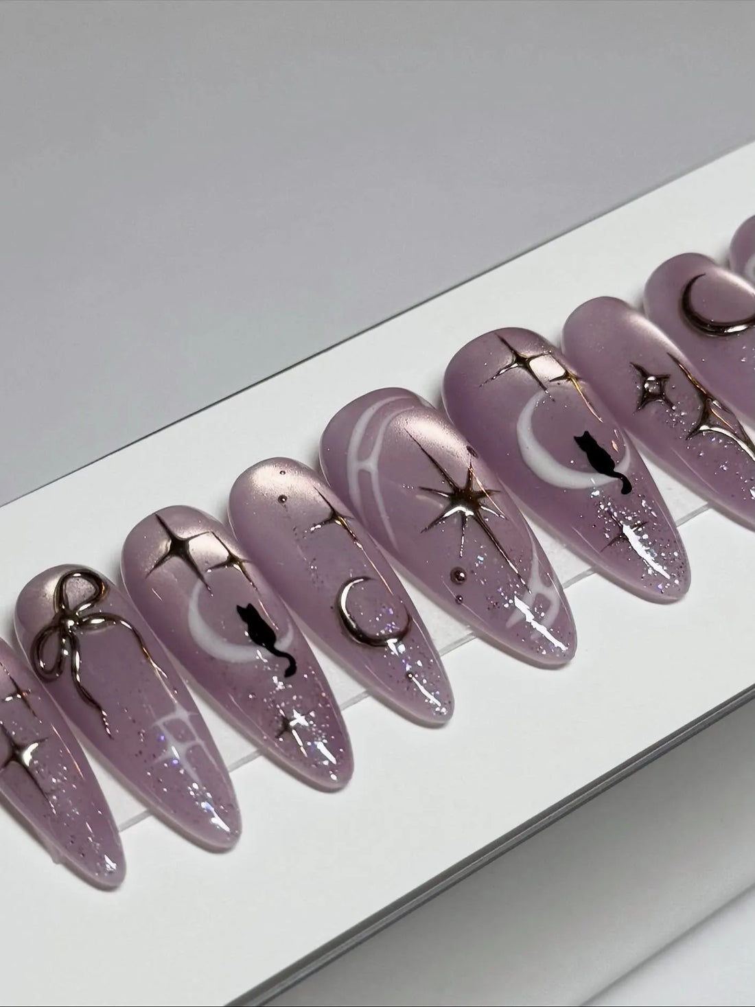 Handmade iridescent purple stiletto press-on nails with celestial moon, star, and cat designs