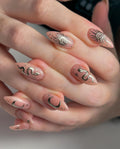 Hand with almond-shaped press-on nails featuring gold sun, moon, and snake celestial designs.