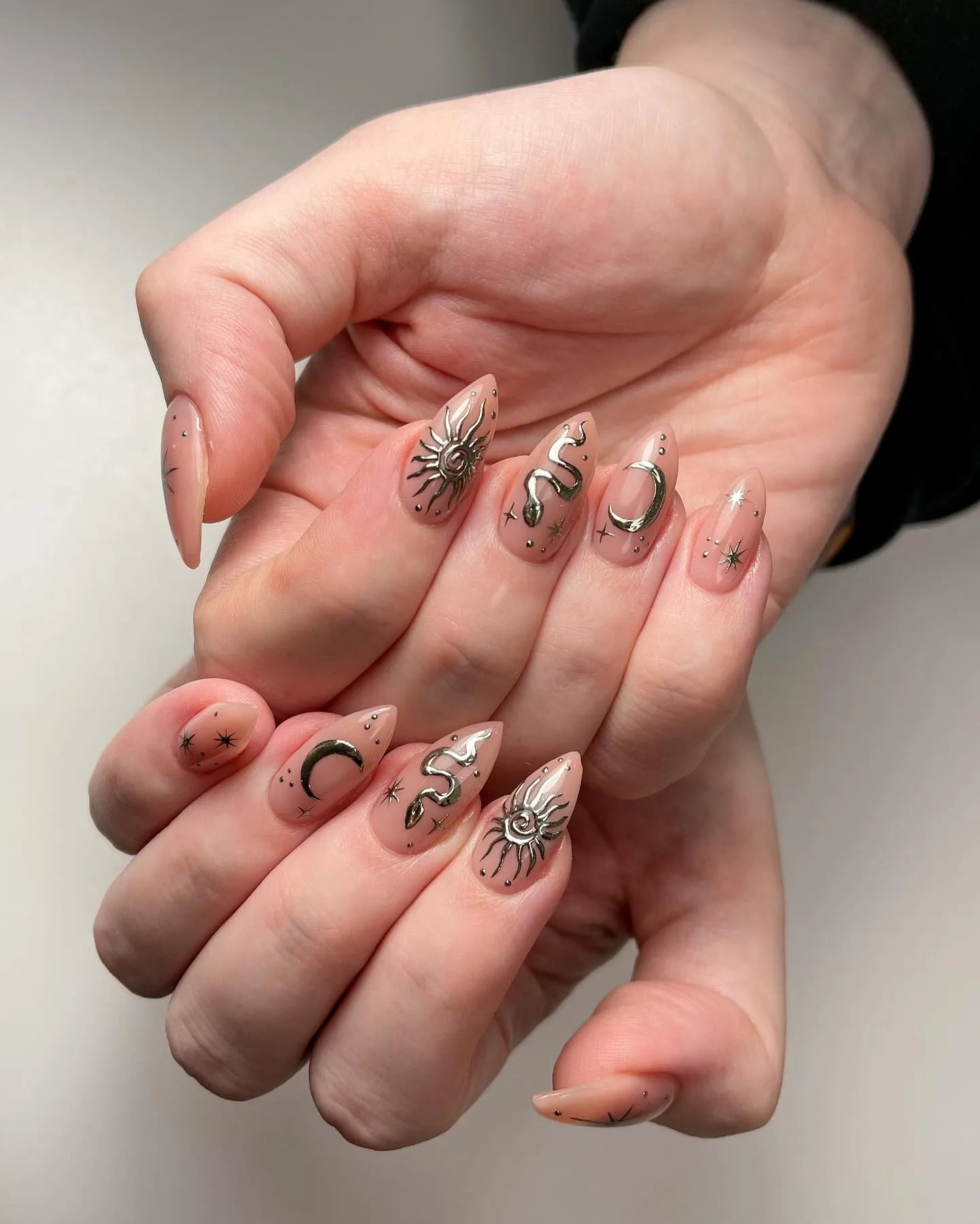 Hand with neutral press-on nails featuring gold sun, moon, snake, and star celestial designs