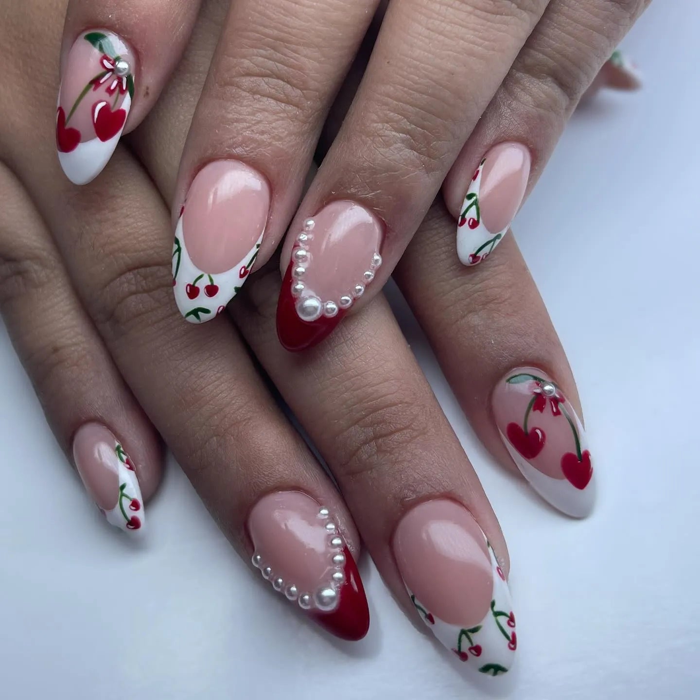 Handmade press-on nails with cherry heart art, red French tips, and pearl accents.