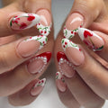 Handmade press-on nails with cherry heart tips, pearl accents, and red French tip art.