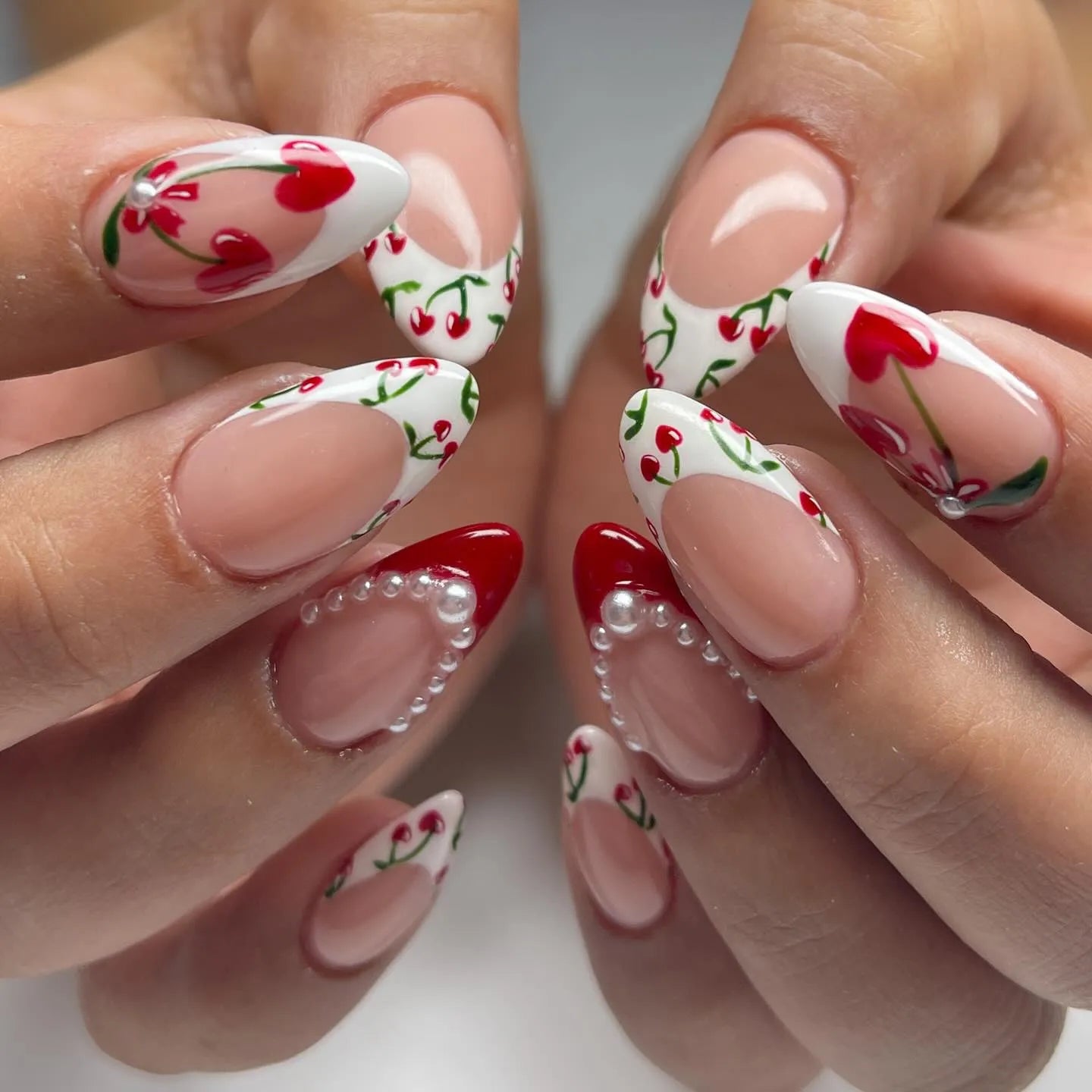 Handmade press-on nails with cherry heart tips, pearl accents, and red French tip art.