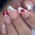 Hand with handmade press-on nails, cherry heart art, red French tips, and pearl accents.