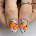 Handmade press-on nails with orange citrus fruit art and blue dotted accents