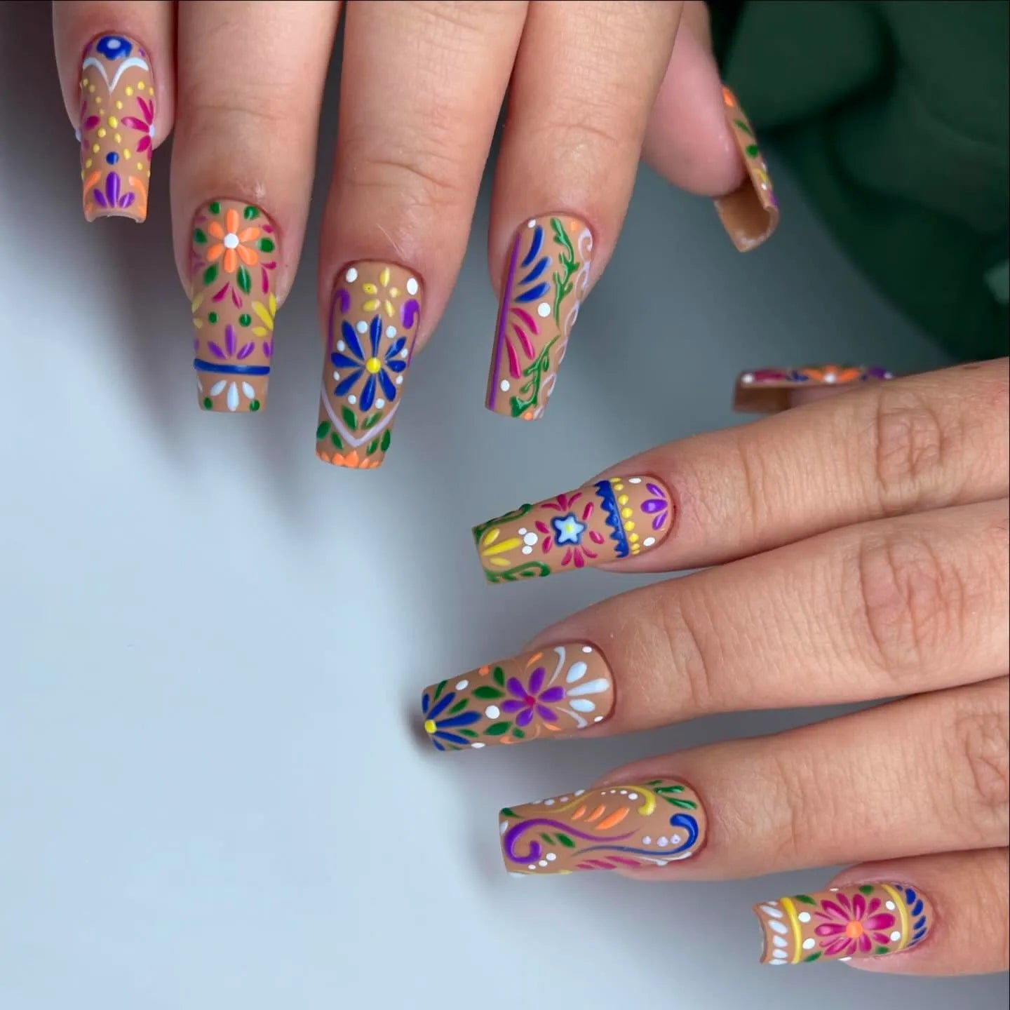 Hand with reusable press-on nails featuring colorful folk art floral designs, summer style