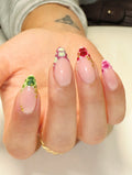 Hand with handmade press-on nails featuring colorful reptile print French tips and gold studs