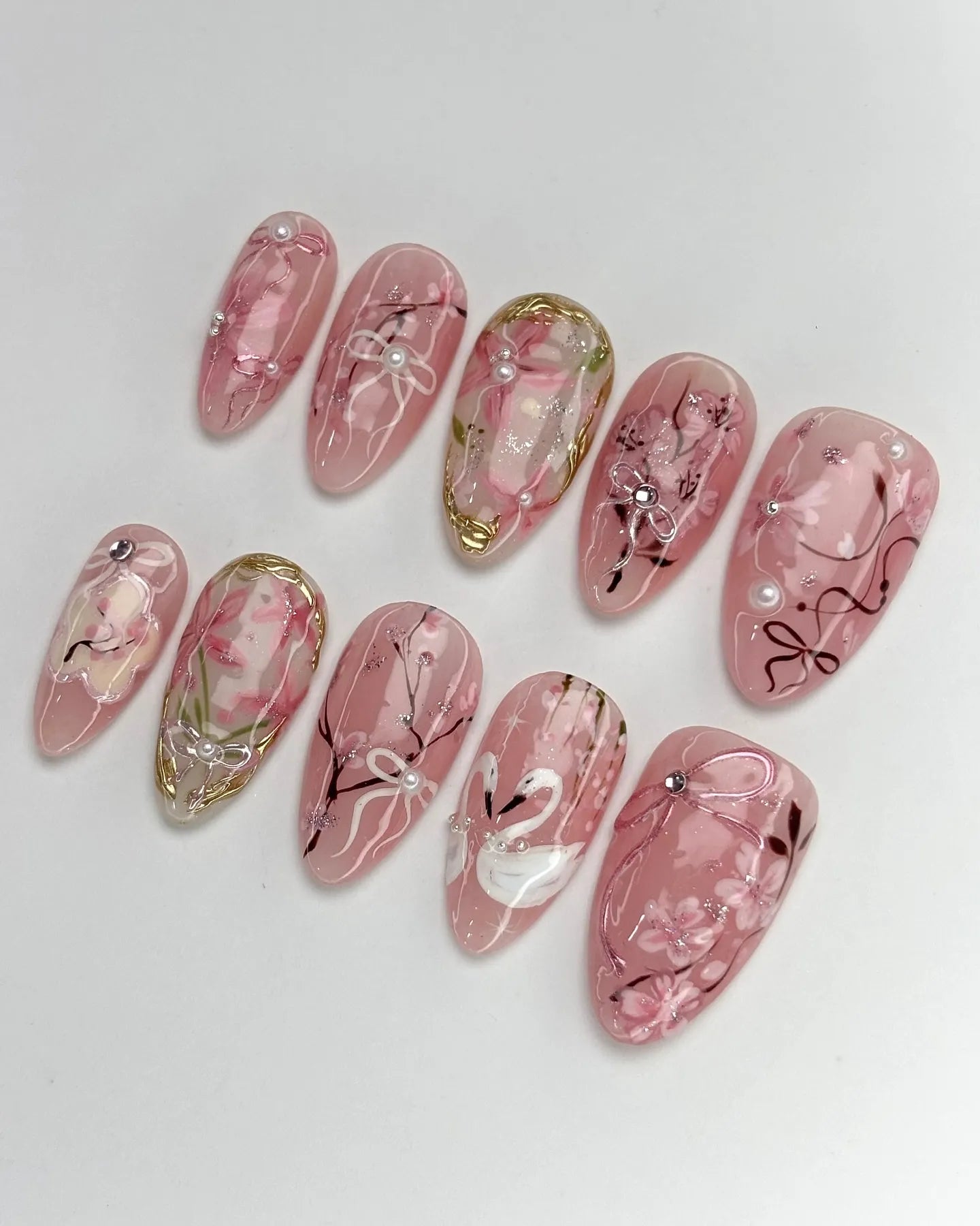 Handmade pink press-on nails with swan, cherry blossom, ribbon, pearl, and gold accents