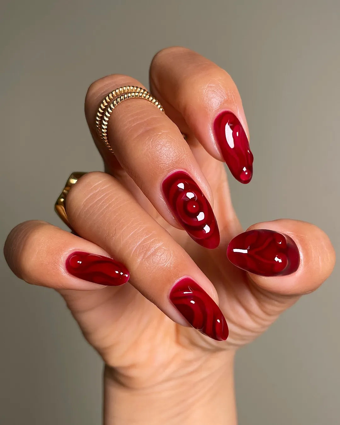 Hand with handmade crimson red swirl 3D press-on nails, glossy finish, almond shape