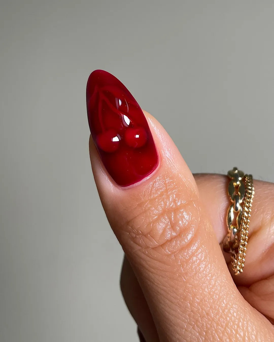 Hand with handmade crimson red swirl 3D press-on nails, glossy finish, almond shape