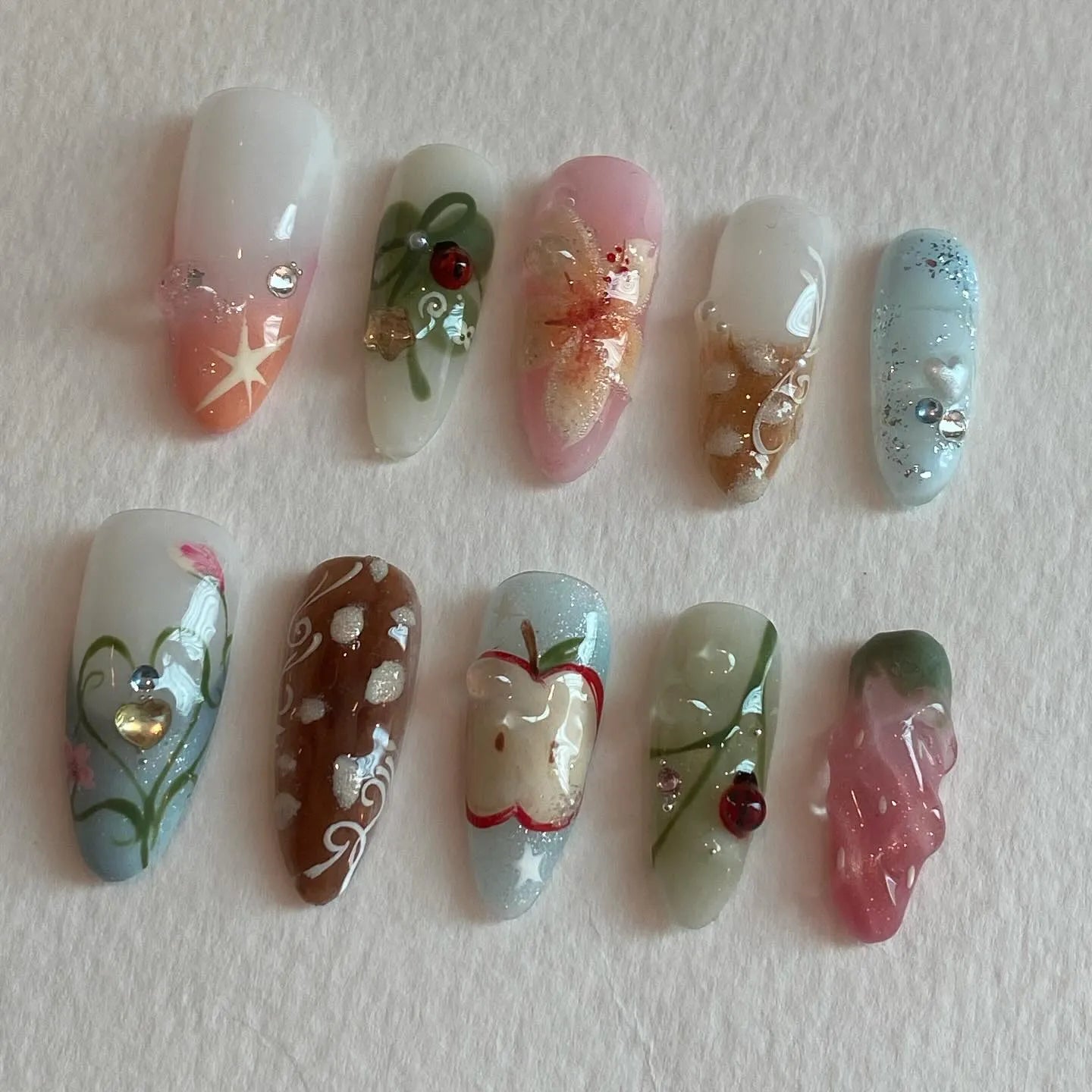 Handmade press-on nails with summer fruit, ladybug, apple, floral, and whimsical picnic designs.