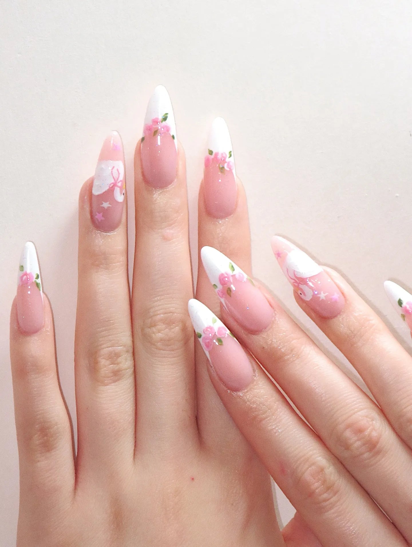 Hand with almond-shaped press-on nails featuring white swan, pink rose, and floral balletcore designs.