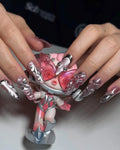 Hand with stiletto metallic press-on nails in chrome pink and silver 3D flower design, holding a matching pink and silver doll.