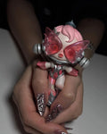 Hand with chrome pink stiletto press-on nails holding a pink and silver futuristic toy figure.