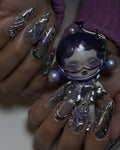 Hand with chrome purple petal 3D metallic stiletto press-on nails holding a space-themed doll