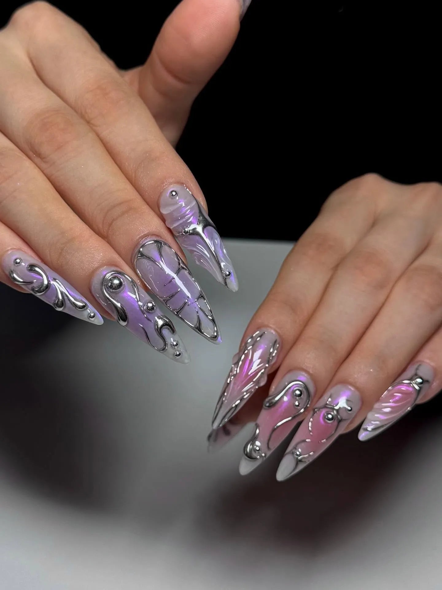 Hand with long stiletto press-on nails in silver and lavender ombre cyberpunk design