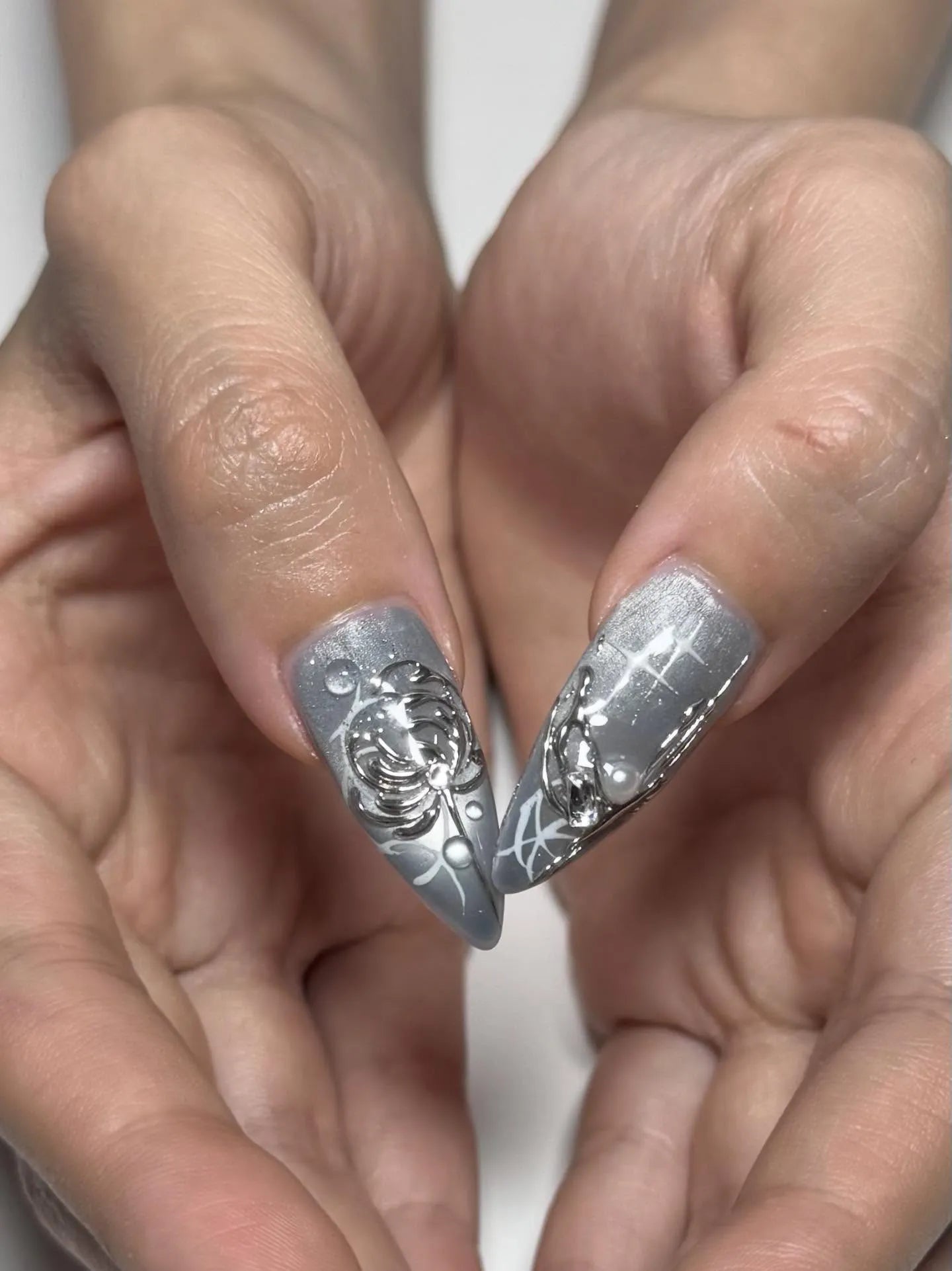 Hand holding silver metallic celestial press-on nails with 3D heart and star accents