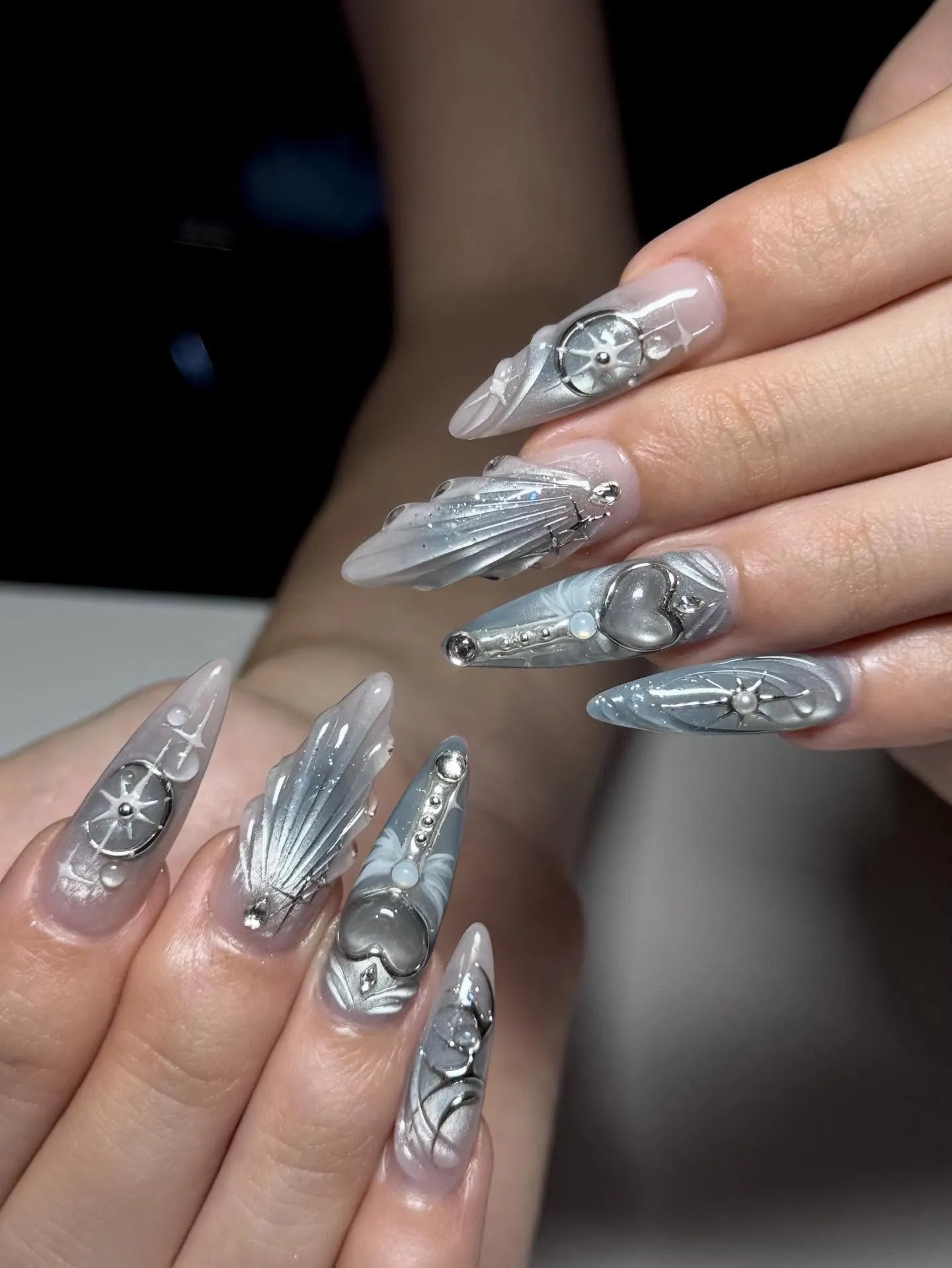 Handmade silver celestial press-on nails with metallic heart and star designs.