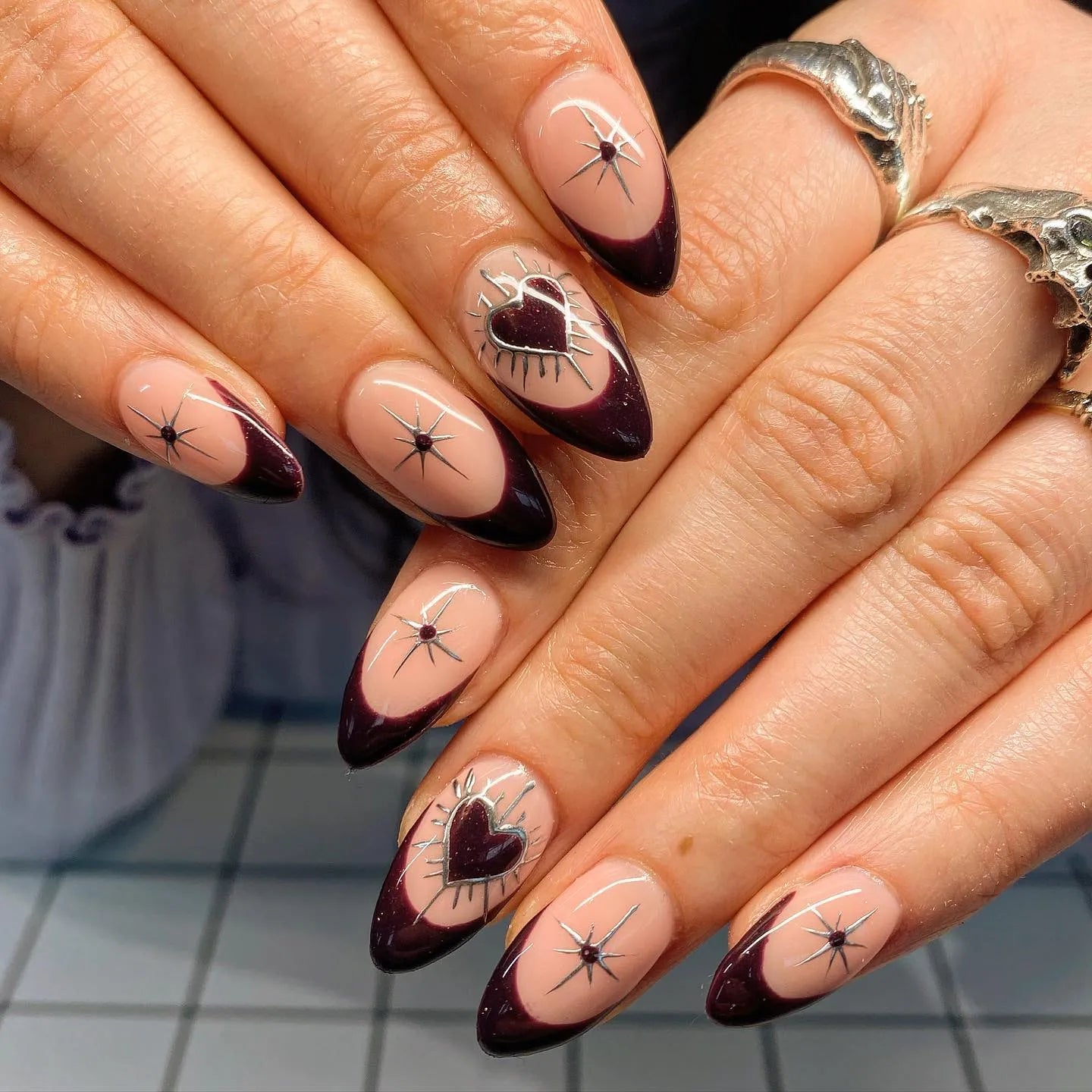 Handmade press-on nails with dark burgundy French tips, silver chrome heart and star accents.