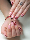 Hand with almond-shaped press-on nails featuring dark cherry French tips, floral and tiger print accents.
