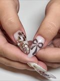 Handmade press-on nails with metallic bow and gold floral 3D designs on almond tips