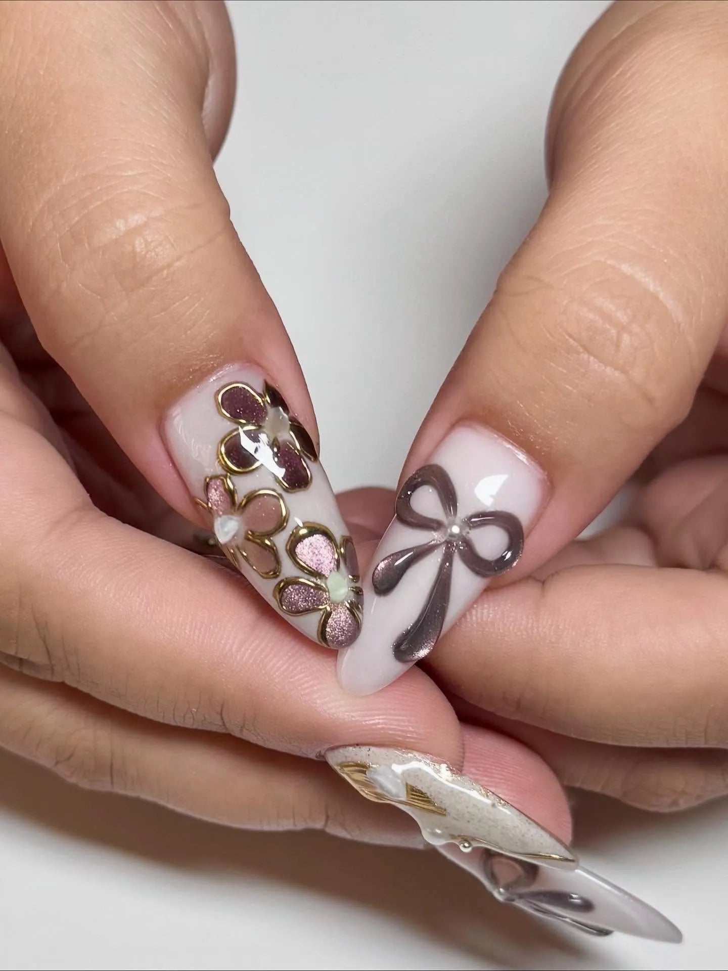 Handmade press-on nails with metallic bow and gold floral 3D designs on almond tips