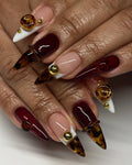 Hand with extra long stiletto press-on nails in ruby red and tortoiseshell, 3D gemstone accents