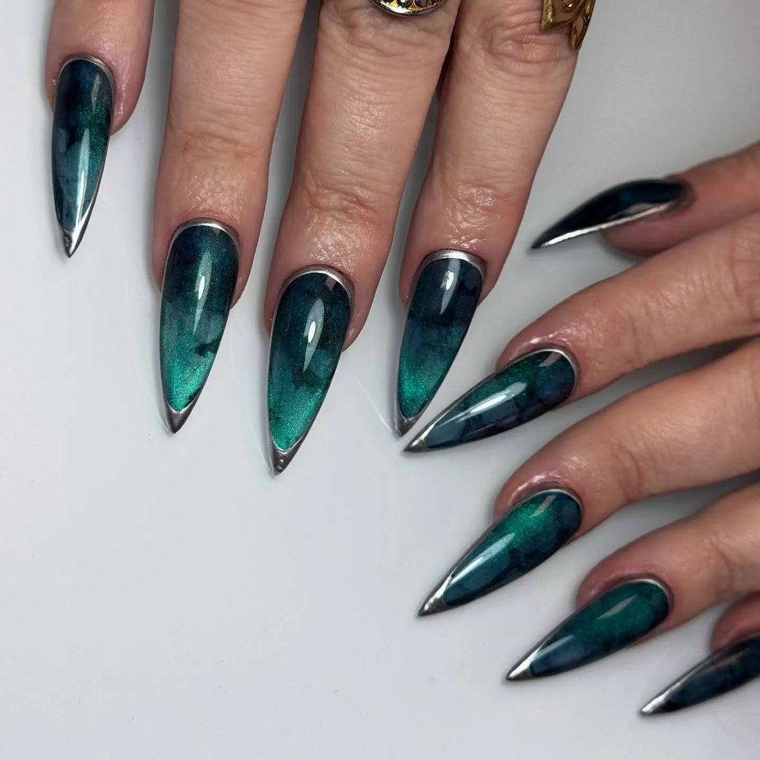 Handmade deep teal nebula press-on nails with silver metallic pointed tips, stiletto shape