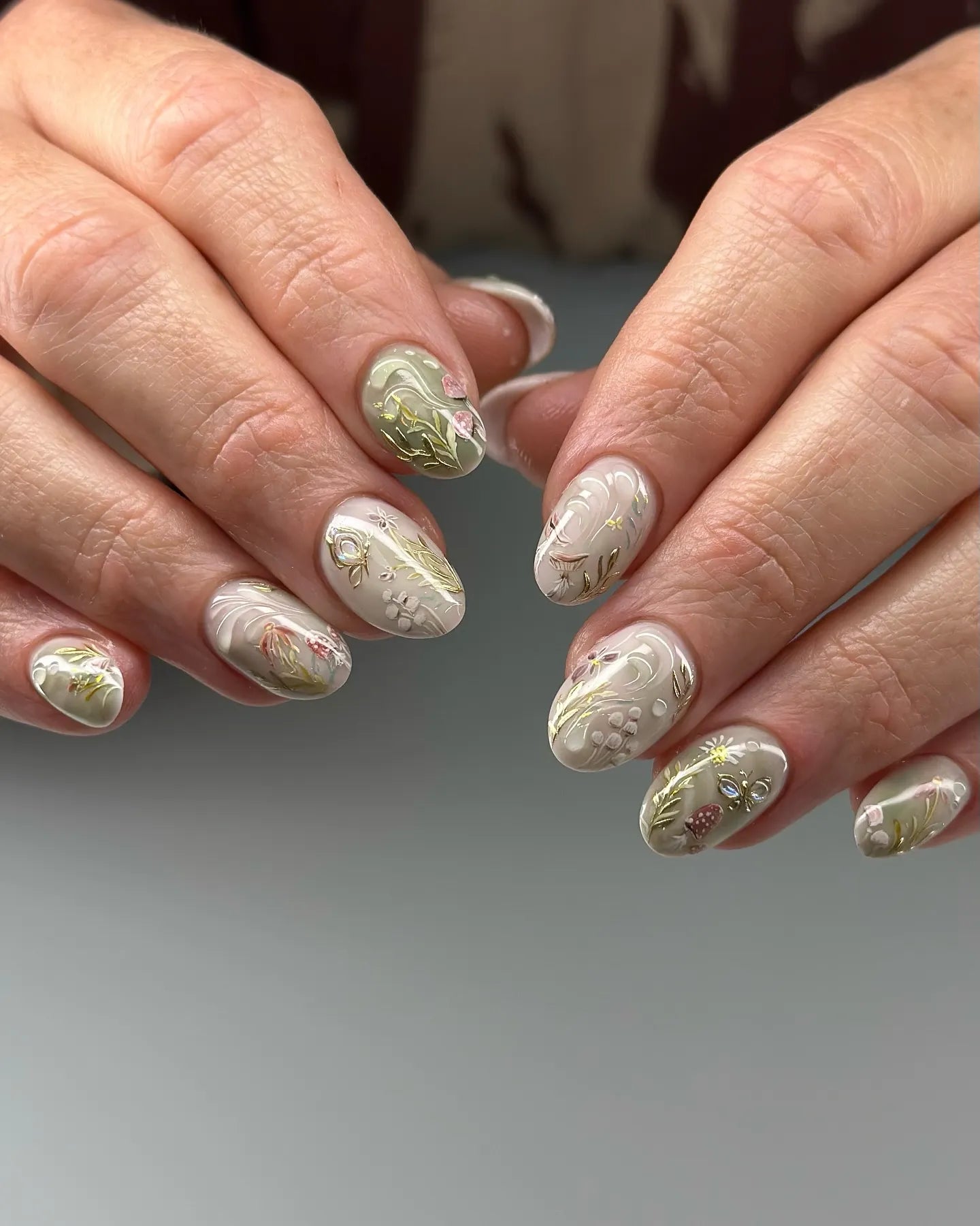 Handmade press-on nails with gilded mushroom and floral forest designs on oval tips.