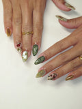 Hand with almond-shaped press-on nails in green, gold, and rose vine designs