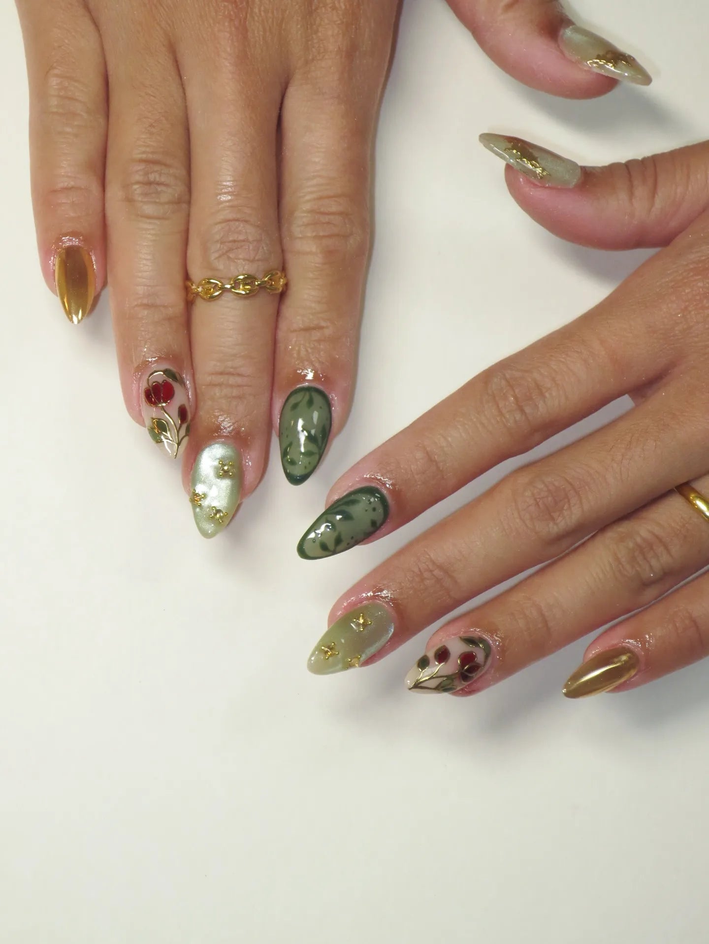 Hand with almond-shaped press-on nails in green, gold, and rose vine designs