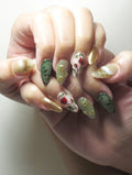 Hand with handmade green, gold, and floral rose vine press-on nails featuring cat eye accents.