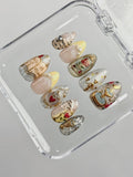 Handmade fairytale press-on nails with gold, rose, heart, and storybook designs in a case